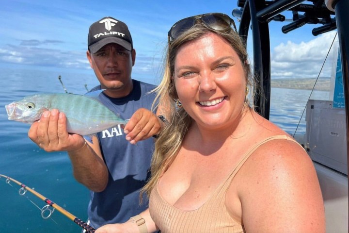 a woman holding a fish on a boat posing for the camera